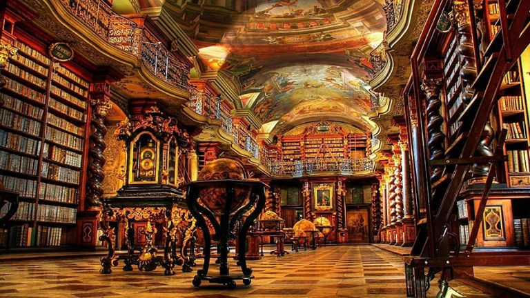 Interior da biblioteca Clementinum. Em primeiro plano um globo terrestre e ao fundo prateleiras de livros. Teto com pinturas e afrescos.